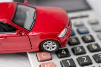 Um carro em cima de uma calculadora representando como economizar no seguro auto.