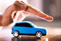 O que o seguro auto cobre representado por um carro sendo protegido com uma mão.
