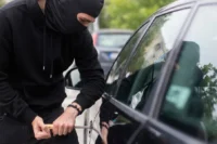 Aumento de roubo de automóveis representado por um homem roubando um carro.