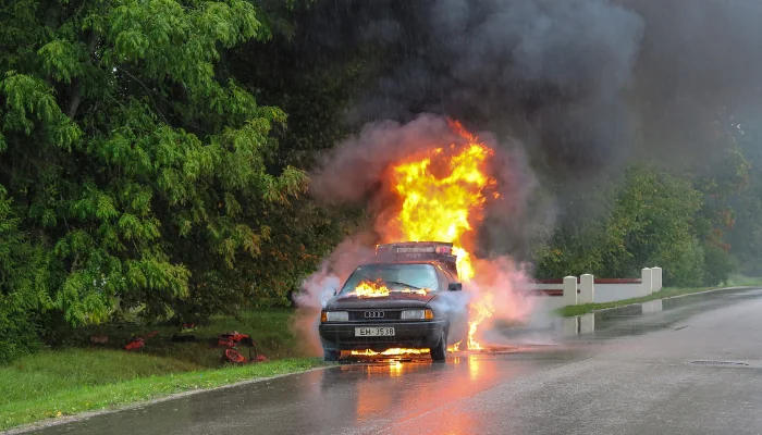 O que fazer quando o carro pega fogo representado por um carro pegando fogo na estrada.