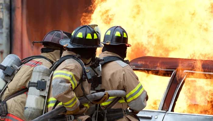 Seguro de carro cobre incêndios causados por vandalismo representado por bombeiros tentando apagar o incêndio de um carro.
