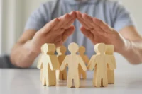 Fatos e mitos sobre seguros representada por símbolos de pessoas sendo protegido por duas mãos.