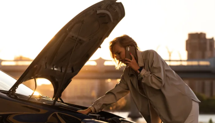 Como Acionar a Cobertura de Despesas Extraordinárias representado por uma mulher olhando o motor do carro e ligando para alguém.