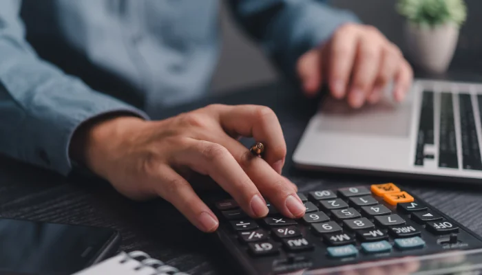 Multas e Penalidades por Atrasos no Pagamento do IPVA 2014 representado por uma pessoa fazendo contas e um computador.