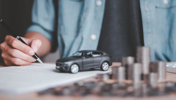 Como Escolher a Seguradora Certa Baseada em Reputação e Avaliações representado por um carrinho com moedas ao lado e uma pessoa com uma caneta em mãos.