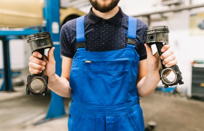 Garantia de peças automotivas: mecânico segura dois pistões de motor.