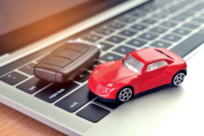 Miniatura de carro na cor vermelha e chave de carro em cima de teclado de notebook, representando como licenciar o carro pela internet.