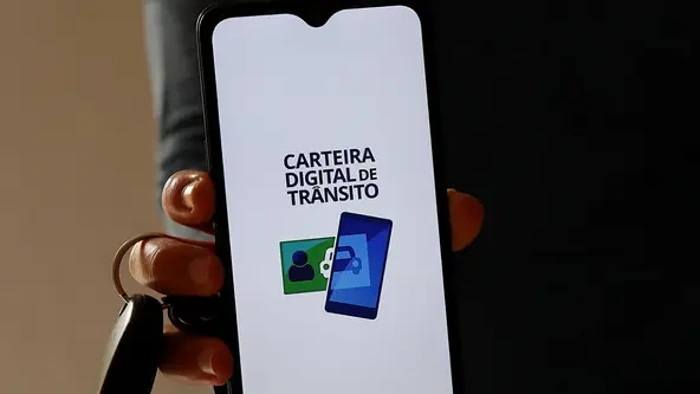 Pessoa segura celular com a mão, onde há um símbolo da Carteira de Trânsito Digital na tela, representando como licenciar o carro pela internet.
