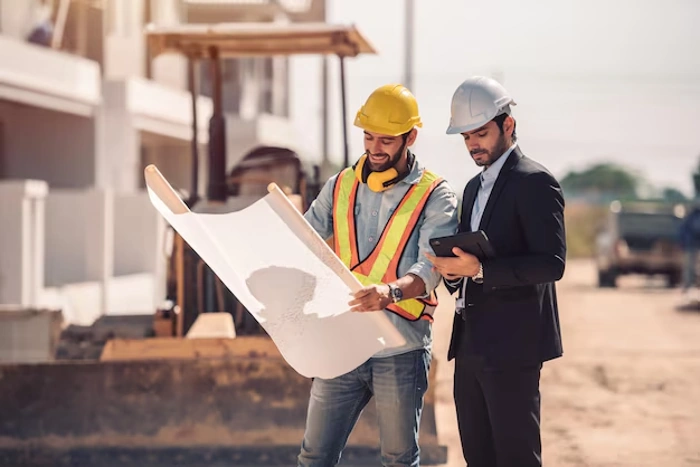 Dois engenheiros discutem algo ao observar projeto de engenharia dentro de um canteiro de obras. Representando seguro de vida para engenheiros.