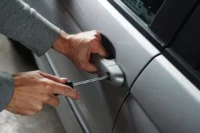 As mãos de uma pessoa com uma chave de fenda na fechadura de um veículo prata para representar a palavra-chave carros menos roubados em sp.