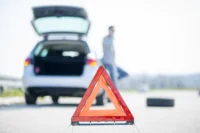 Motorista sinaliza a via após uma necessidade de assistência. Há um triângulo de sinalização no chão. Falando sobre assistência 24 horas.