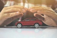 Pessoa com mãos sobre miniatura de carro na cor vermelha. Falando sobre os carros usados mais seguros do brasil.