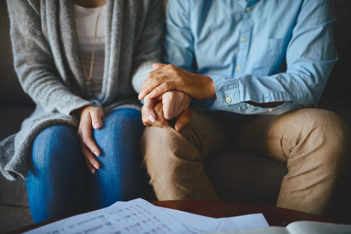 Casal dá as mãos. Não é possível ver os rostos, mas é possível ver que estão sentados. Falando sobre seguro de vida para idosos.