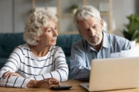Casal de idosos analisa condições de seguro de vida em um notebook. Falando sobre seguro de vida para idosos.