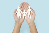 Pessoa segura figura em papel que representa família na palma das mãos. Falando sobre indenização do seguro de vida.