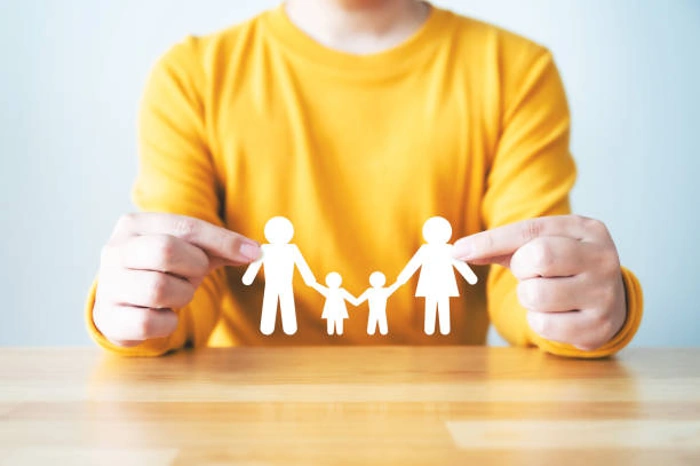 Indivíduo segura figura impressa que representa família utilizando as pontas dos dedos. Falando sobre seguro de vida de 500 mil.