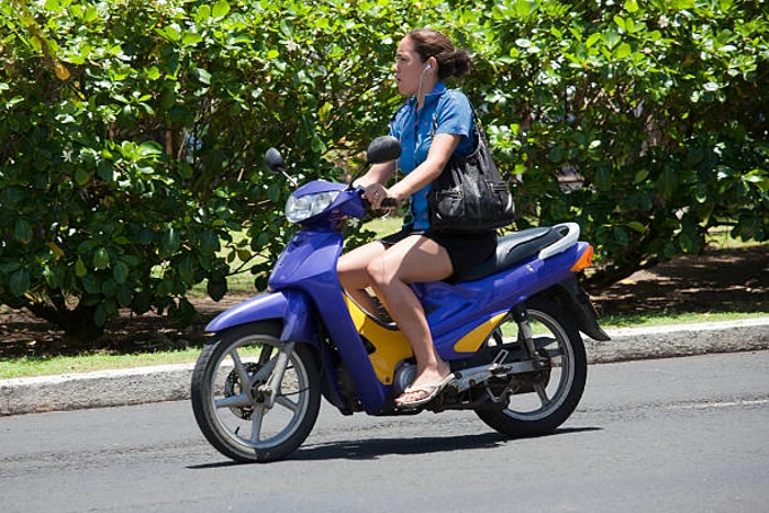 Mulher pilotando moto 50cc na cor azul. Explicando acima de quantas cilindradas precisa de cnh.