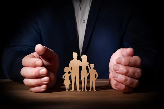 Homem sentado posiciona as mãos em volta de figura que representa uma família. Falando sobre seguro de vida em grupo empresarial.