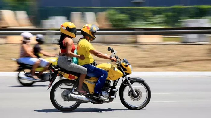 Homem pilotando moto e levando mulher na garupa. A moto tem a cor amarela. Explicando acima de quantas cilindradas precisa de cnh.