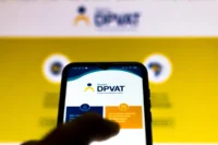Pessoa com celular na mão. A logomarca do seguro DPVAT está na tela. Ao fundo, há uma imagem desfocada que também remete ao DPVAT. Falando sobre seguro dpvat valor da indenização.