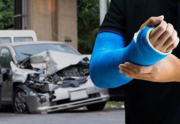 Pessoa com braço na tipóia em primeiro plano, enquanto carro acidentado está em segundo plano. Explicando sobre "sofri um acidente de carro tenho direito ao dpvat".