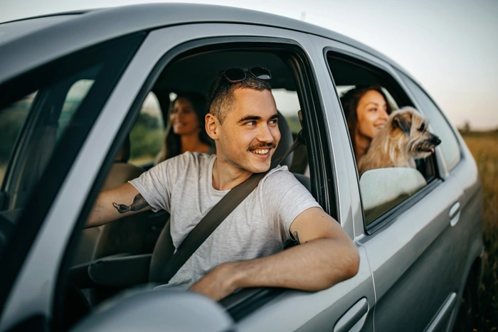 Pessoas sorridentes sentadas em interior de carro olham para o exterior do veículo. Falando sobre seguro de carro barato.