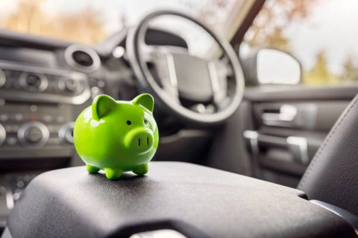Cofre em formato de porquinho na cor verde em cima de banco de carro. Explicando quanto custa um seguro de carro por mês.