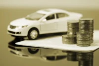 Miniatura de carro branco ao lado de pilhas de moedas. Falando sobre seguro de carro barato.