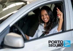 Mulher sorridente dentro do seu carro exibe algumas chaves. A logomarca da Porto Seguro está na imagem. Falando sobre os benefícios seguro auto porto seguro.