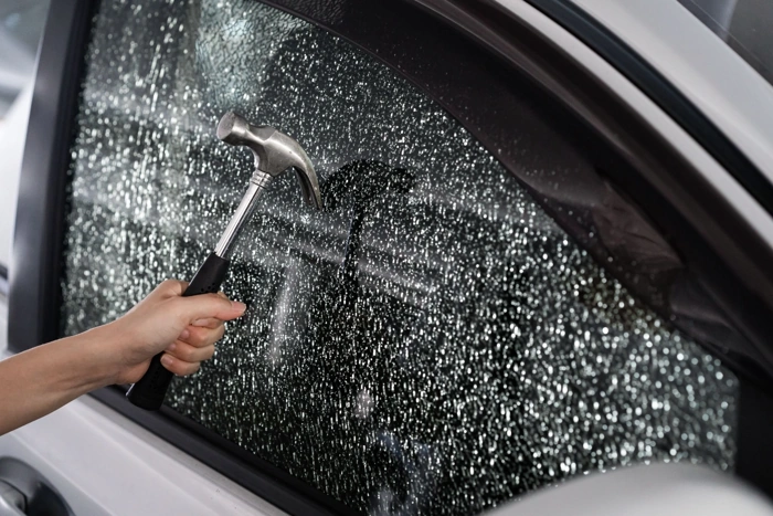 Pessoa faz teste em vidro blindado com martelo. Explicando se seguro de carro blindado é mais caro.