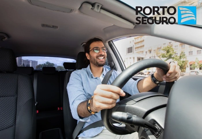 Homem sorridente dirige o seu carro. Falando sobre os benefícios seguro auto porto seguro.