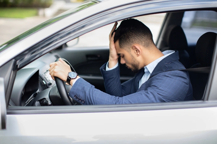 Homem leva mão à testa enquanto segura o volante do seu carro. Ensinando como perder o medo de dirigir.