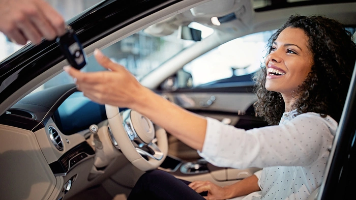 Mulher sorridente pega chaves de carro enquanto está sentada em seu veículo. Ensinando como perder o medo de dirigir.