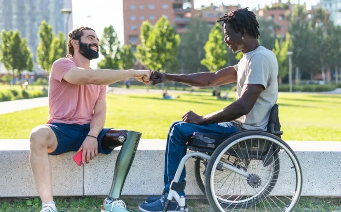 Dois homens portadores de deficiência física se cumprimentam em área de jardim. Falando sobre o seguro auto para deficientes.