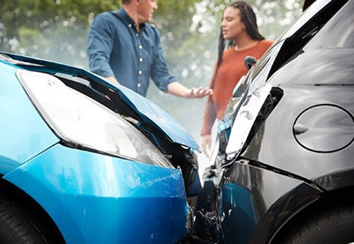 Em primeiro plano, uma colisão entre dois carros. Em segundo plano, um homem e uma mulher discutem. Falando sobre indenização parcial do veículo.