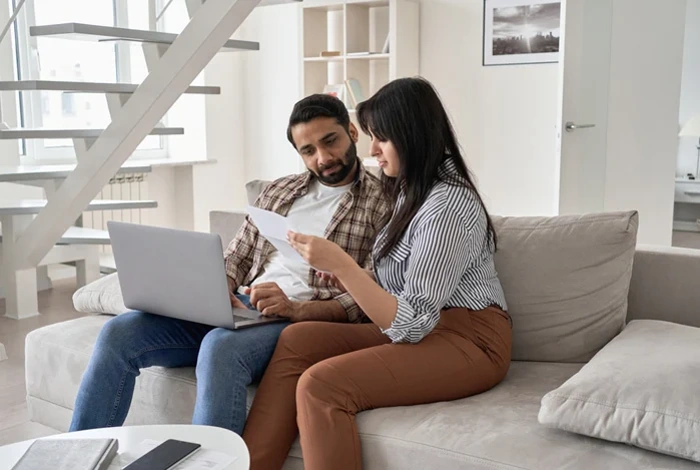 Homem e mulher analisam apólice de seguro. Há um notebook sobre uma mesa. Falando sobre apólice de seguro auto.