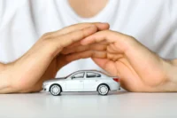 Pessoa faz sinal de cobertura sobre miniatura de carro na cor prata. Falando sobre o seguro auto popular.